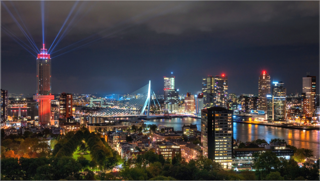 Nachtfoto van De Zalmhaven in Rotterdam met rode lichtstralen, Erasmusbrug en verlichte skyline – spectaculaire stadsfotografie.
