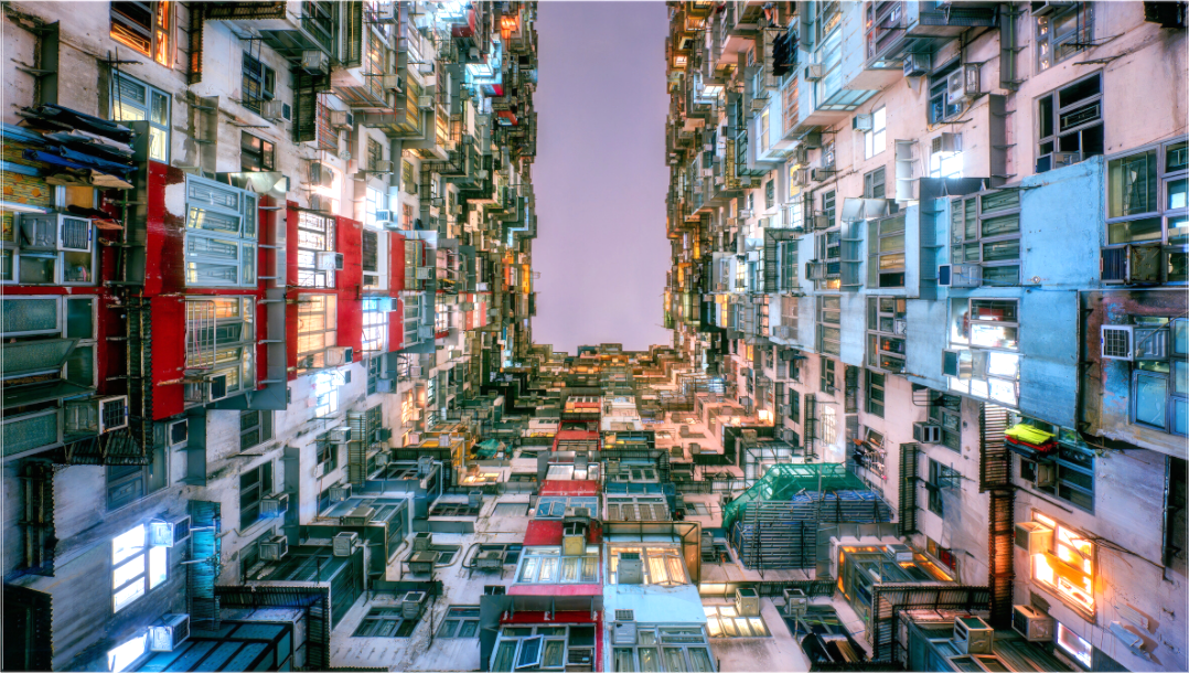 Uitzicht omhoog in Hongkongse wooncorridor met hoge dichtheid en kleurrijke gevels – verticale stadsarchitectuur.
