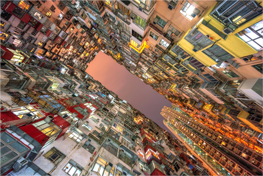 Uitzicht omhoog in Hongkongse binnenplaats bij nacht met kleurrijke gevels, kunstlicht en zachte luchtgloed – stedelijke dichtheid.