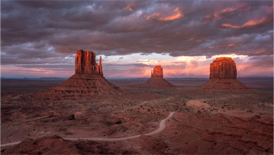Monument Valley met drie zandstenen buttes bij zonsondergang en dramatische wolkenlucht – woestijnfotografie.